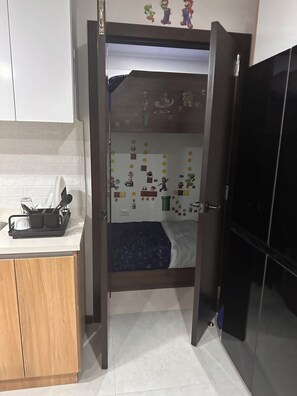 A room with a bed, a small kitchenette, and a door leading to another room.