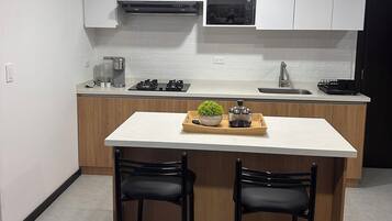 Une cuisine moderne avec des meubles blancs, un îlot central doté de tabourets de bar et un four à micro-ondes placé au-dessus de l’évier.