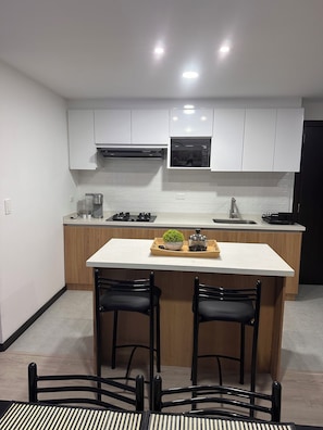 A modern kitchen with white cabinets, a central island with bar stools, and a microwave above the sink. - Fantastic 2-bedroom apartment in Cuenca Kid Bunk Room, private parking and pool (Cuenca)