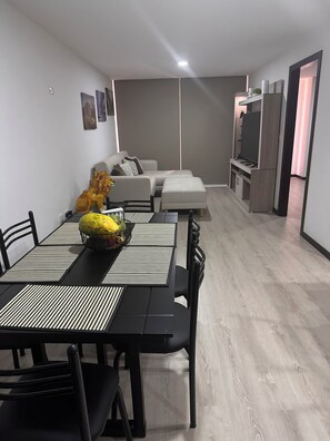 A modern living room with a sofa, a dining table with chairs, and a TV stand.