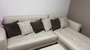 Ein Ecksofa mit passendem Hocker, gemusterten Kissen und einer schlichten Wand im Hintergrund.