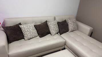 Un canapé modulable assorti d’un pouf, agrémenté de coussins à motifs, avec un mur uni en arrière-plan.