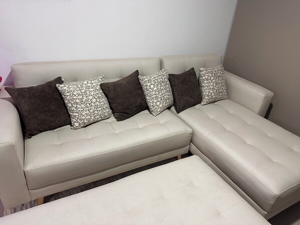 A sectional sofa with a matching ottoman, patterned pillows, and a plain wall in the background.