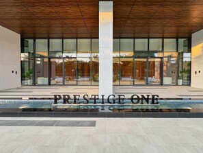 A modern building entrance with a large sign reading 'PRESTIGE ONE' and a pool area in front. - Top Floor 2BR | Golf View | Vista Sports City (Dubai)