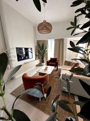A modern living room with a flat-screen TV, a sofa, a coffee table, and a red armchair. - Stunning 1-Bedroom Apartment | Full Marina View (Dubai)