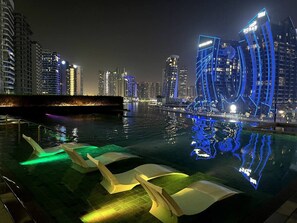 Eine beleuchtete Stadtlandschaft bei Nacht mit glitzerndem Wasserspiegel und moderner Sitzgelegenheiten.