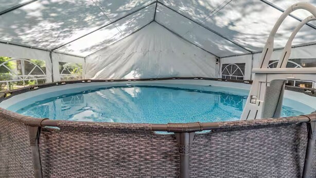 A covered swimming pool with a diving board and wicker chairs. - New Home 3-bed 3-bath w/pool, golfcart and bounce house (North Myrtle Beach)