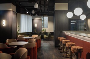 Ein modernes Interieur mit runden Tischen, gepolsterten Sitzgelegenheiten, Pendelleuchten und einer Bar.