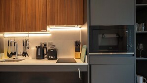 Moderni keittiö, jossa on puukalusteet, sisäänrakennettu mikroaaltouuni, vedenkeitin ja erilaisia keittiövälineitä.