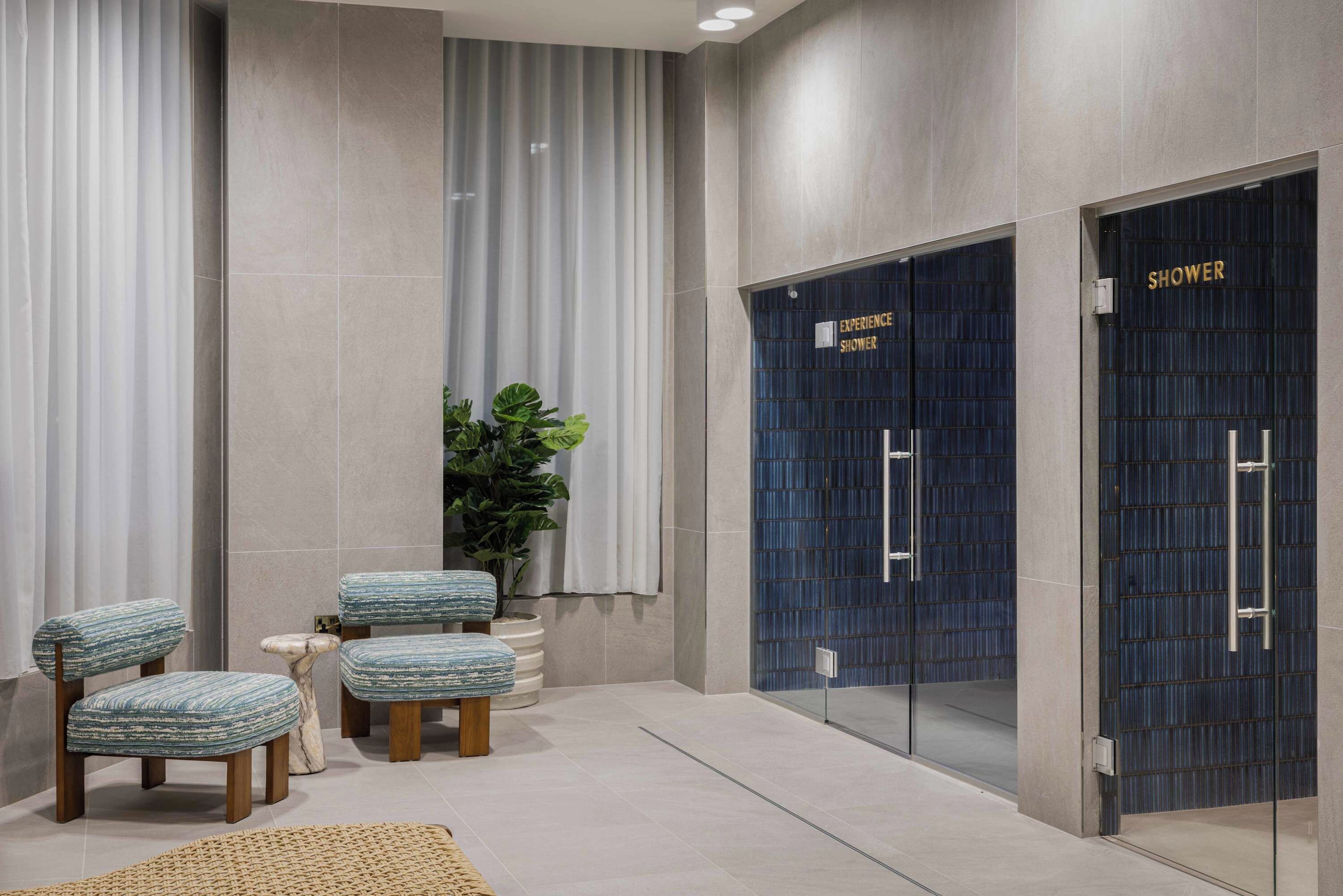 A modern bathroom with two blue shower doors, a potted plant, and two upholstered chairs.
