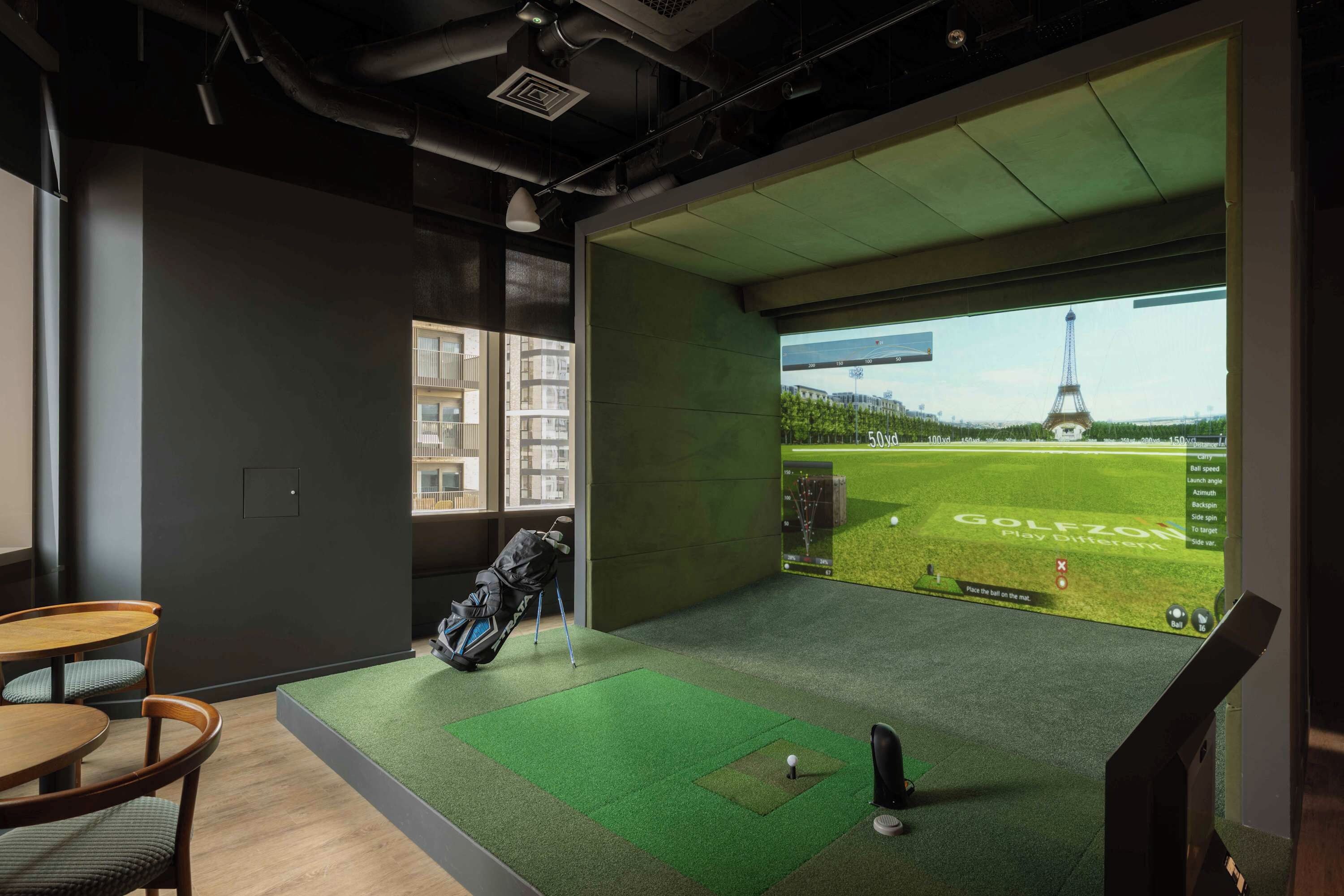 A room with a golf simulation setup, a view of the Eiffel Tower, and a seating area with a table and chairs.