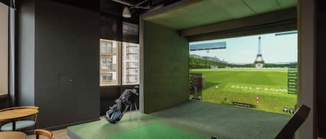 A room with a golf simulation setup, a view of the Eiffel Tower, and a seating area with a table and chairs.