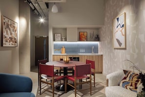 A modern interior with a round dining table, red chairs, a blue sofa, and a patterned wall. - Contemporary Studio | Cowork + Gym | StayCozy (London)