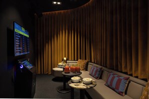 A dimly lit room with a large screen displaying a music playlist, a sofa with cushions, a small round table with drinks and snacks, and a control panel with a circular light. - Contemporary Studio | Cowork + Gym | StayCozy (London)