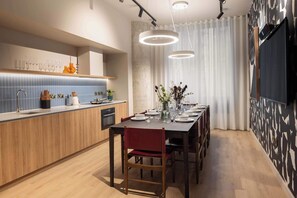 A modern kitchen with a wooden countertop, a dining area with a table set for four, and a large window with curtains. - Contemporary Studio | Cowork + Gym | StayCozy (London)