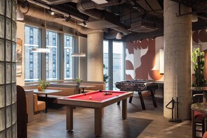 A billiards table, seating area, and a foosball table in a modern indoor space with large windows and industrial design elements. - Roomy Studio Apartment | Gym Access | StayCozy (London)