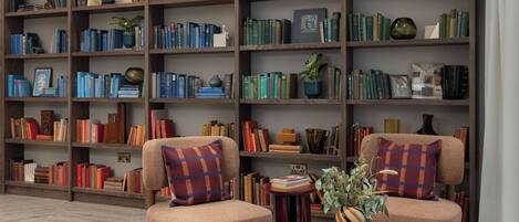 A library with multiple bookshelves, two armchairs, and a coffee table with books and a vase.