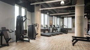 Un gimnasio con equipo de ejercicio, ventanas amplias y un pilar de concreto.