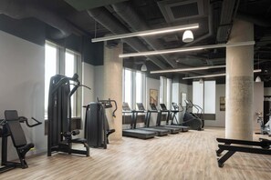 A gym with exercise equipment, large windows, and a concrete pillar. - Roomy Studio Apartment | Gym Access | StayCozy (London)