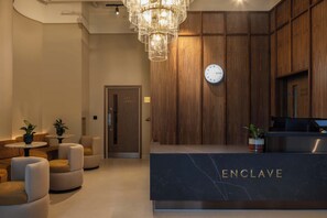 Ein Empfangsbereich mit Marmor-Theke mit der Aufschrift 'ENCLAVE', Holzvertäfelung, einer Uhr und einem Kronleuchter.