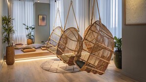 Una habitación con una silla colgante de ratán, una cama con almohadas, una planta en maceta y un cuadro en la pared.