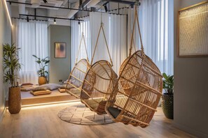A room with a hanging rattan chair, a bed with pillows, a potted plant, and a framed artwork on the wall. - Roomy Studio Apartment | Gym Access | StayCozy (London)