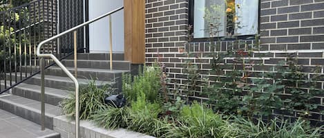 A staircase leading to a brick building with a metal handrail and a window with a view of greenery.
