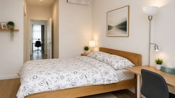A bedroom with a bed, bedside tables, a desk, a chair, a lamp, and a picture on the wall.