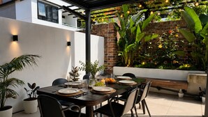 Un espacio exterior para comer con pared de ladrillo, plantas en macetas y un banco.