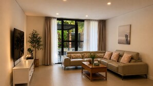 Una sala de estar con sofá, mesa de centro, televisor y un ventanal con cortinas.