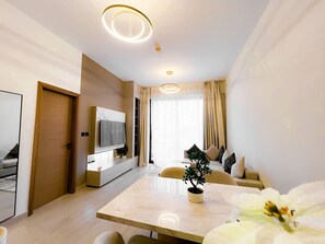 A modern hotel room with a flat-screen TV, a dining table, a sofa, and a potted plant. - Stylish 1-Bedroom Retreat in Prime Gardens | Arjan (Dubai)