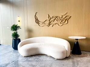 Ein moderner Lounge-Bereich mit einer gebogenen Couch, einem runden Tisch und einem an der Wand befestigten abstrakten Kunstwerk.