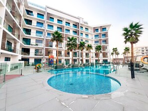 Ein mehrstöckiges Hotel mit einem zentral gelegenen Pool, umgeben von Palmen und Glasgeländern.