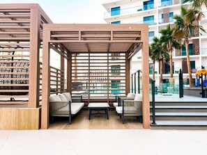 An outdoor seating area with a wooden pergola, cushioned chairs, and a table. - Stylish 1-Bedroom Retreat in Prime Gardens | Arjan (Dubai)
