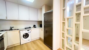 A compact kitchen with white cabinets, a stainless steel refrigerator, a washing machine, and a built-in oven. - Stunning 2BR In Dubai Marina With Amazing views (Dubai)