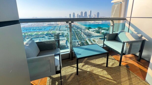 A balcony with a city view, two chairs, a table, and a woven mat. - Stunning 2BR In Dubai Marina With Amazing views (Dubai)