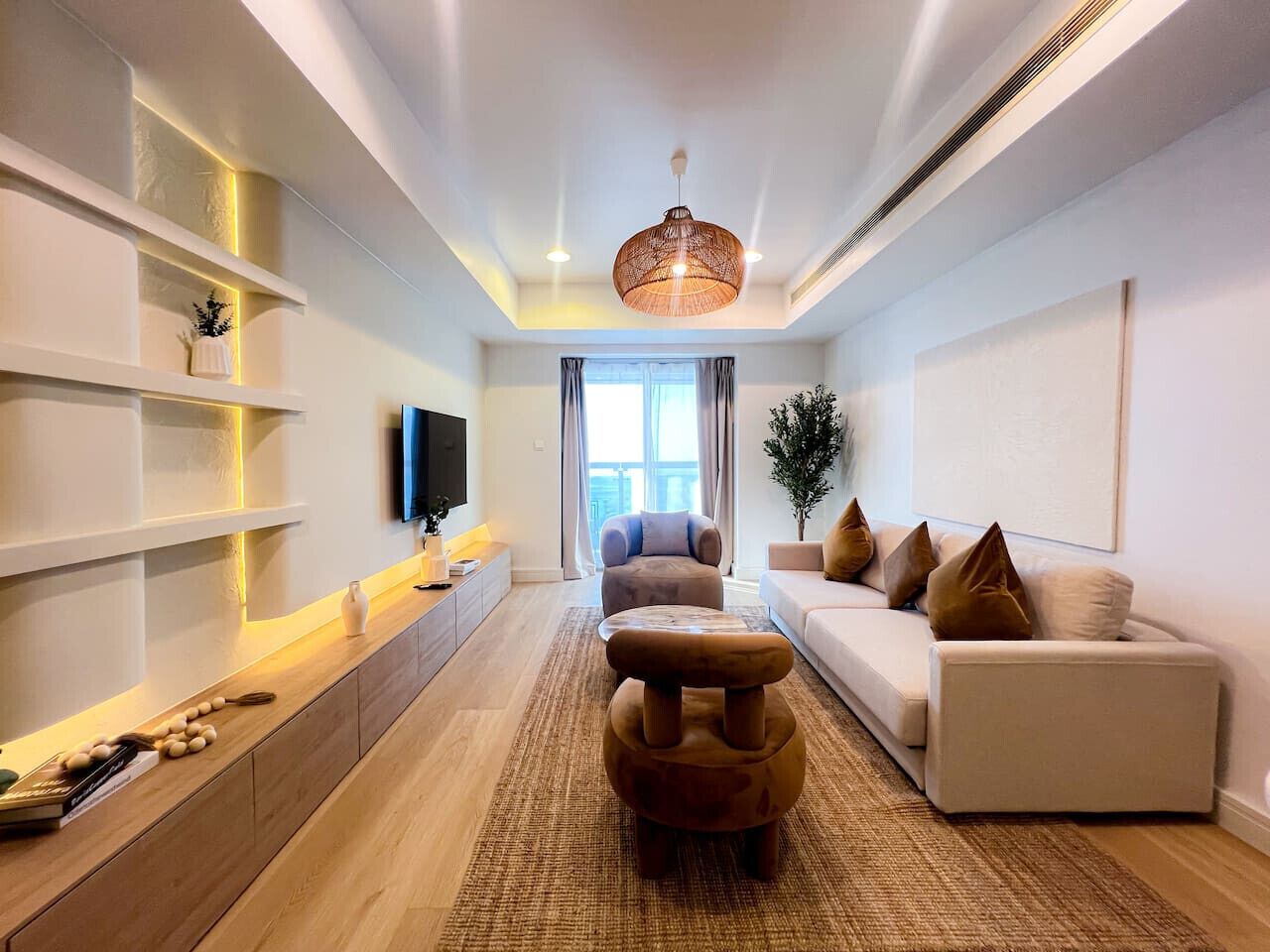 Uma sala de estar moderna com sofá, banquinho e TV de tela plana na parede.