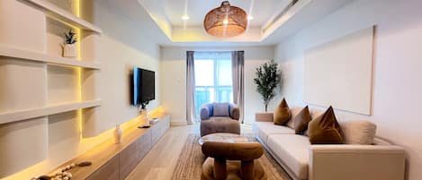 Un salon moderne avec un canapé, un pouf et un téléviseur à écran plat fixé au mur.