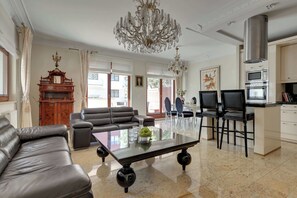 A spacious living room with a chandelier, leather sofas, a dining area with chairs, and a kitchen with modern appliances. - Belle Époque Suite by the Sea | 2 Bedrooms (Gdańsk)