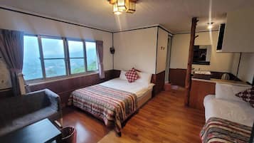 Una habitación con cama, escritorio, silla, mesita y ventana con vista.