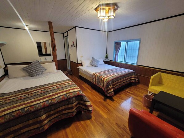 A room with two beds, a wooden floor, a yellow chair, and a window with curtains.