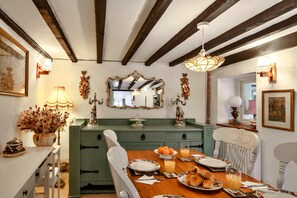 A dining area with a wooden table set for breakfast, a green cabinet, and a mirror above the counter. - Cottage With Inglenook Hearth (Winkleigh)