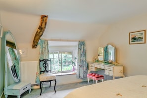 A bedroom with a large bed, a vanity with a mirror, a chair, and a window with curtains. - Cottage With Inglenook Hearth (Winkleigh)