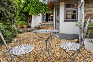 A patio with three metal chairs and a table, surrounded by pebbles. - Cottage With Inglenook Hearth (Winkleigh)
