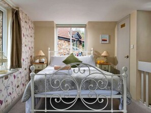 Ein Schlafzimmer mit weißem Metallbettgestell, zwei Nachttischen mit Lampen, einem Fenster mit Vorhängen und einer Tür mit einem Schild.