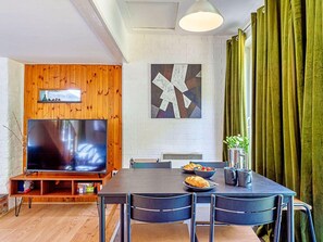 A modern living room with a flat-screen TV, wooden panel wall, abstract art, and a dining area with a table and chairs. - Historic Stay Near Knebworth (Knebworth)