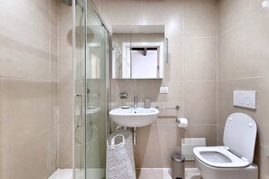 Un baño moderno con cabina de ducha de vidrio, un lavabo blanco y un inodoro.