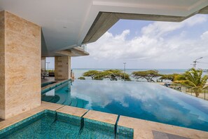 Uma piscina infinita moderna com vista clara do oceano e palmeiras.