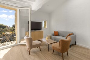 A modern living room with a grey sofa, two armchairs, a wooden coffee table, and a television on a wooden cabinet. - Apt L’Hospital – In the heart of Tourrettes-sur-Loup (Tourrettes-sur-Loup)