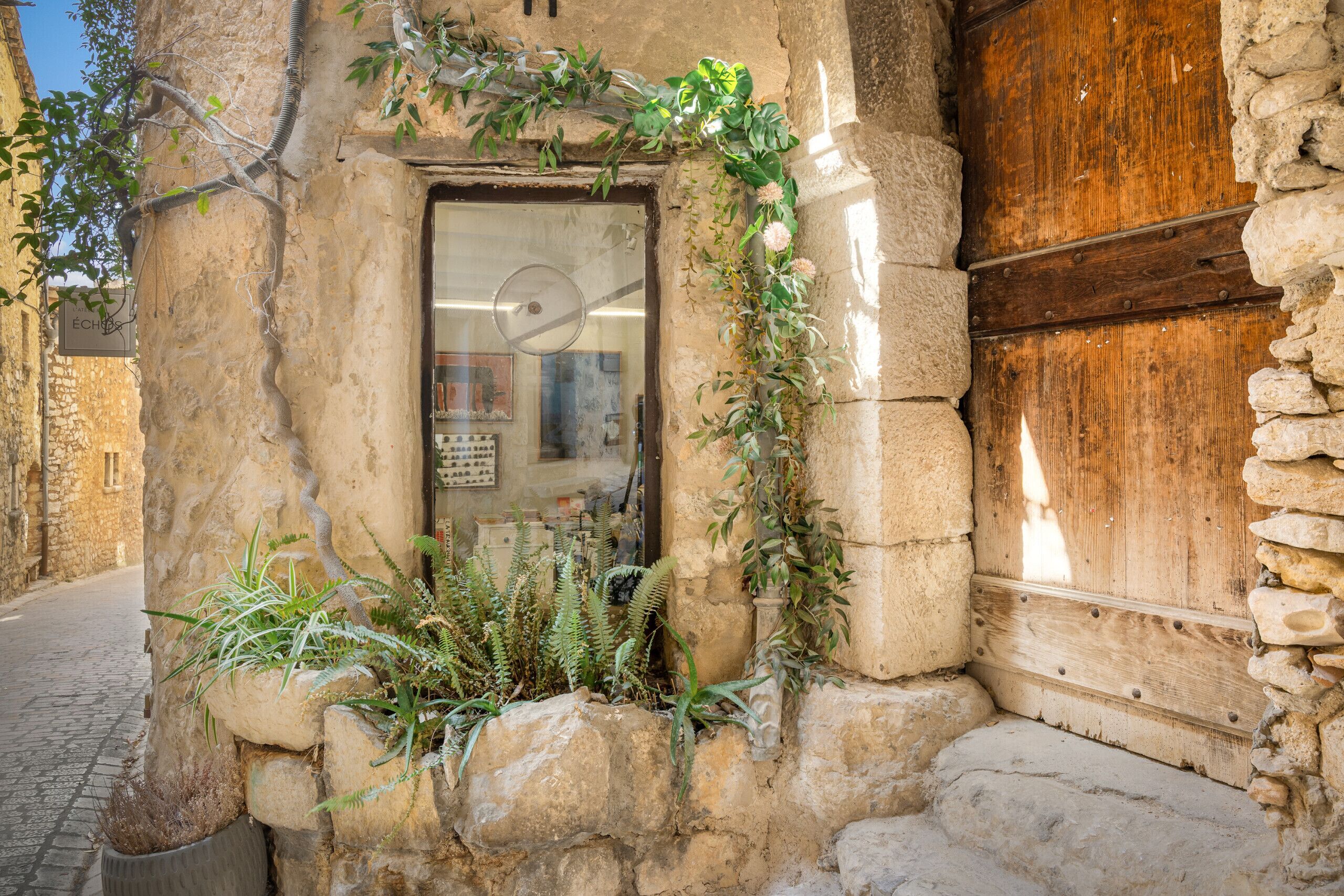 A stone building with a wooden door, a small shop entrance, and greenery growing around the base.